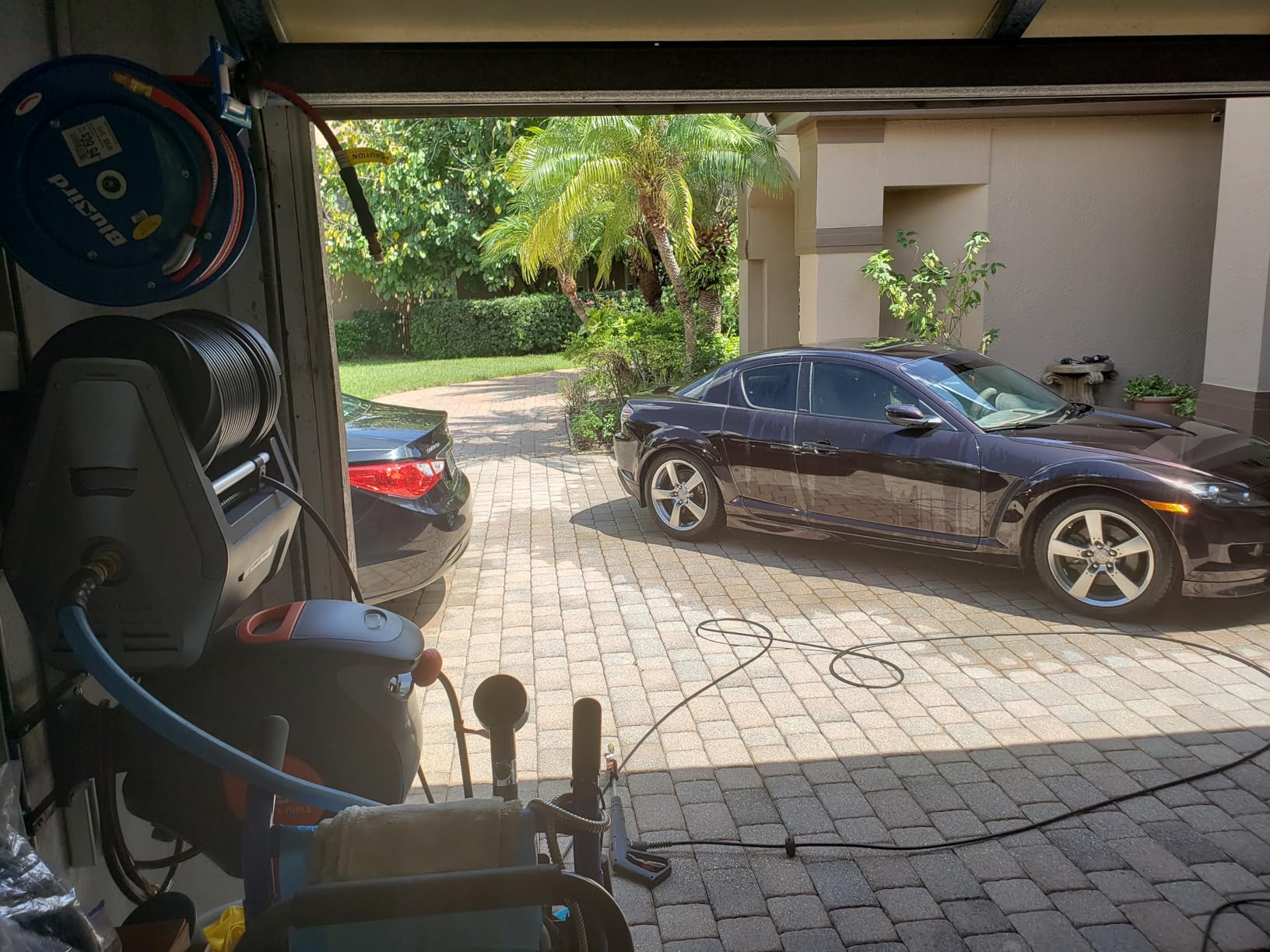 Foto real da mangueira retrátil perto da garagem e do carro